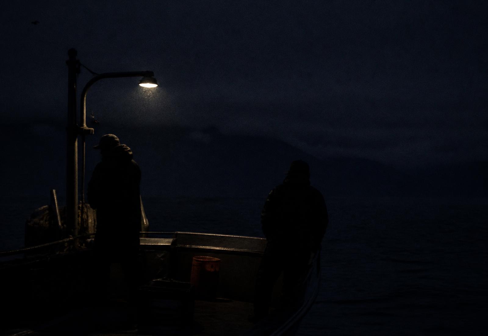 Two fishermen silhouetted on deck under a single light
